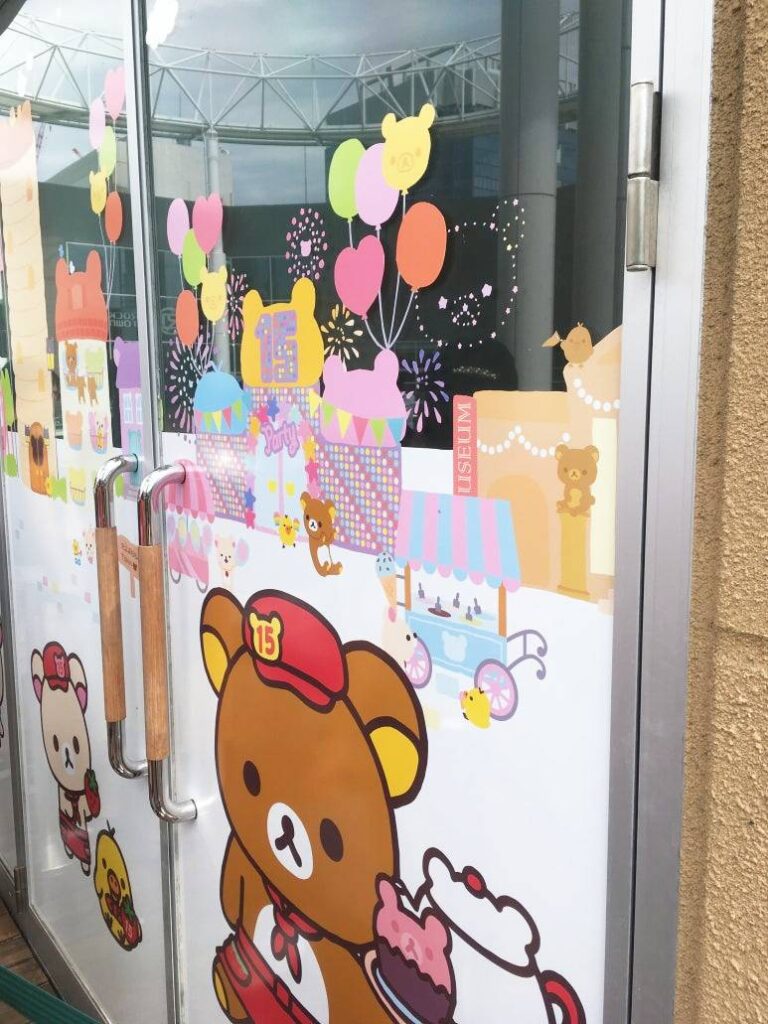 Close-up of the entrance door at the Rilakkuma Café in Osaka, decorated with colorful illustrations celebrating the 15th anniversary