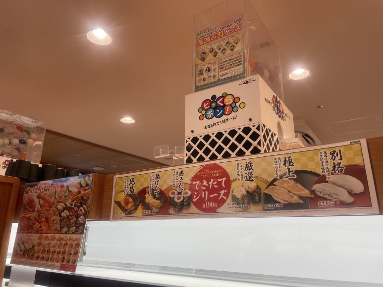 Bikkura Pon capsule toy machine installed above the sushi conveyor at Kura Sushi