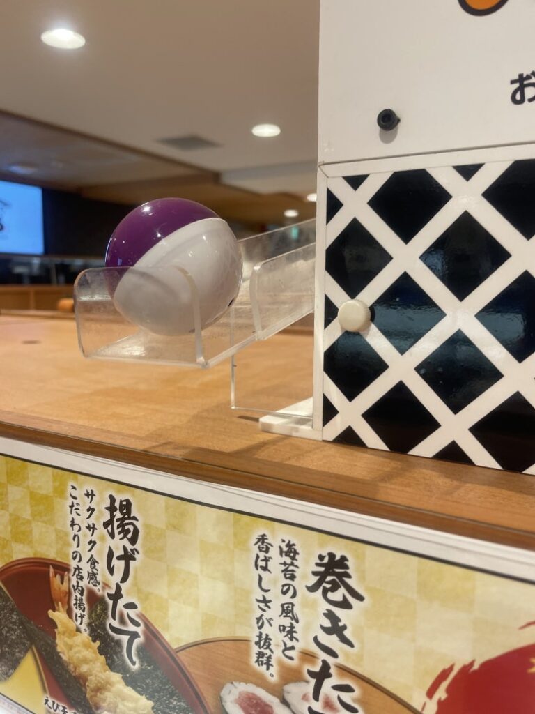 A prize capsule coming out of the Bikkura Pon machine at Kura Sushi