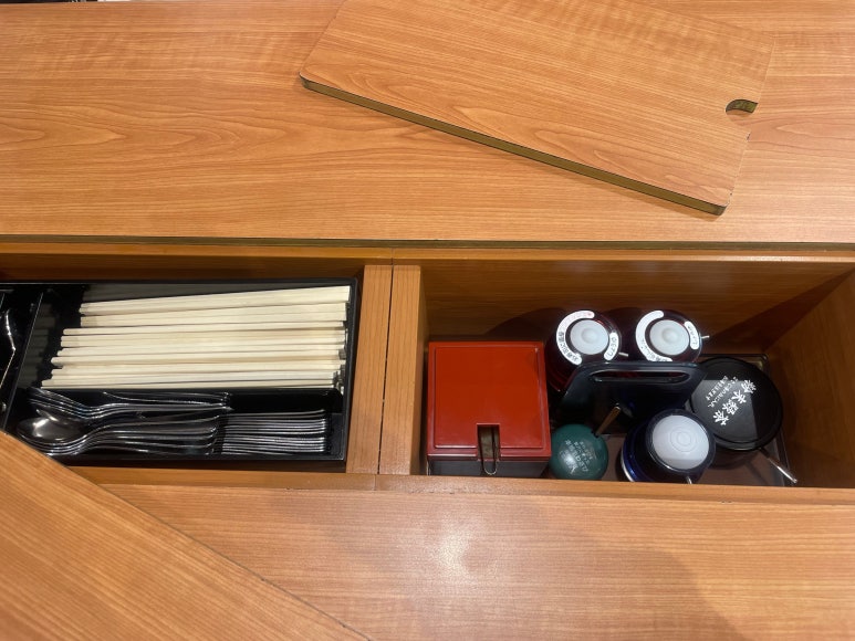Inside the Kura Sushi table compartment with chopsticks, spoons, soy sauce, and condiments