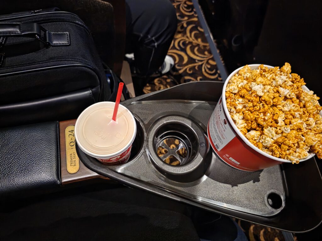 Premium seat tray holding popcorn, drink, and a backpack placed beside the armrest