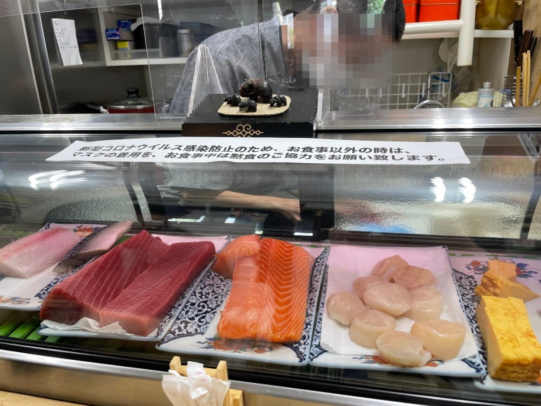 Fresh sashimi ingredients displayed at a seafood donburi shop in Nijo Market, Sapporo, with a chef preparing meals behind the counter