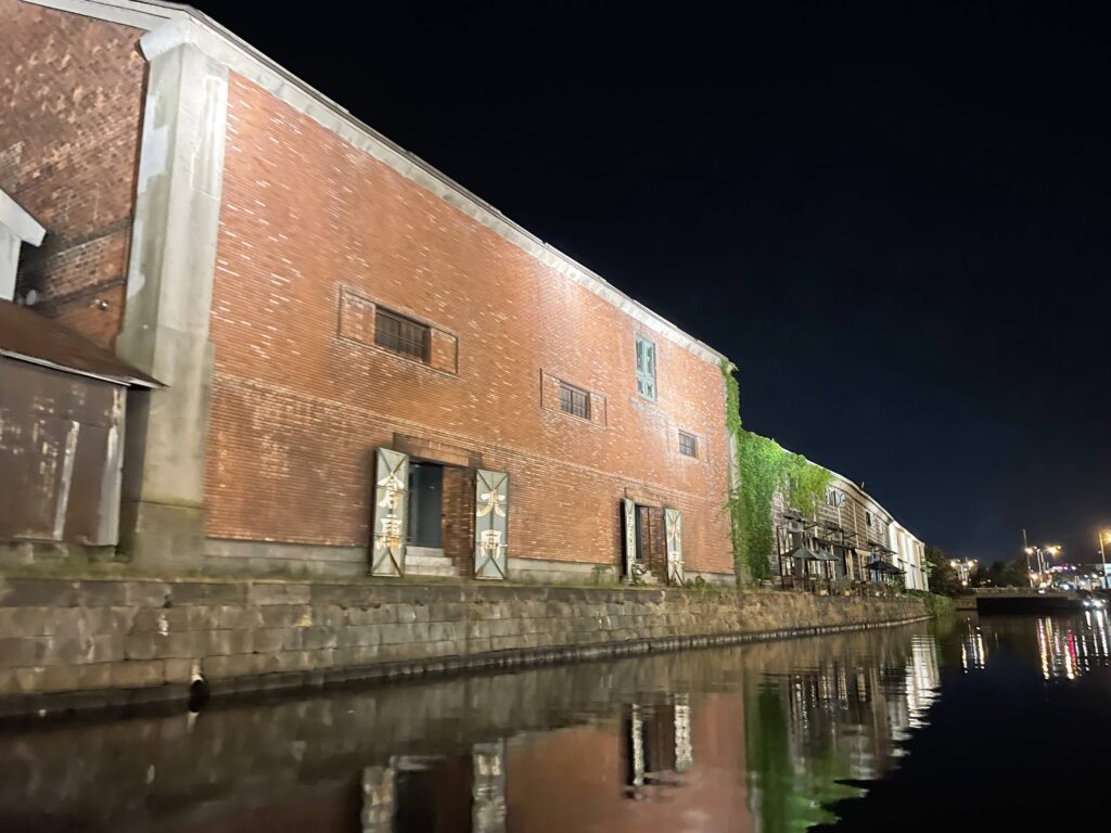 View from a night canal cruise in Otaru, showing a red brick building reflected on the water.