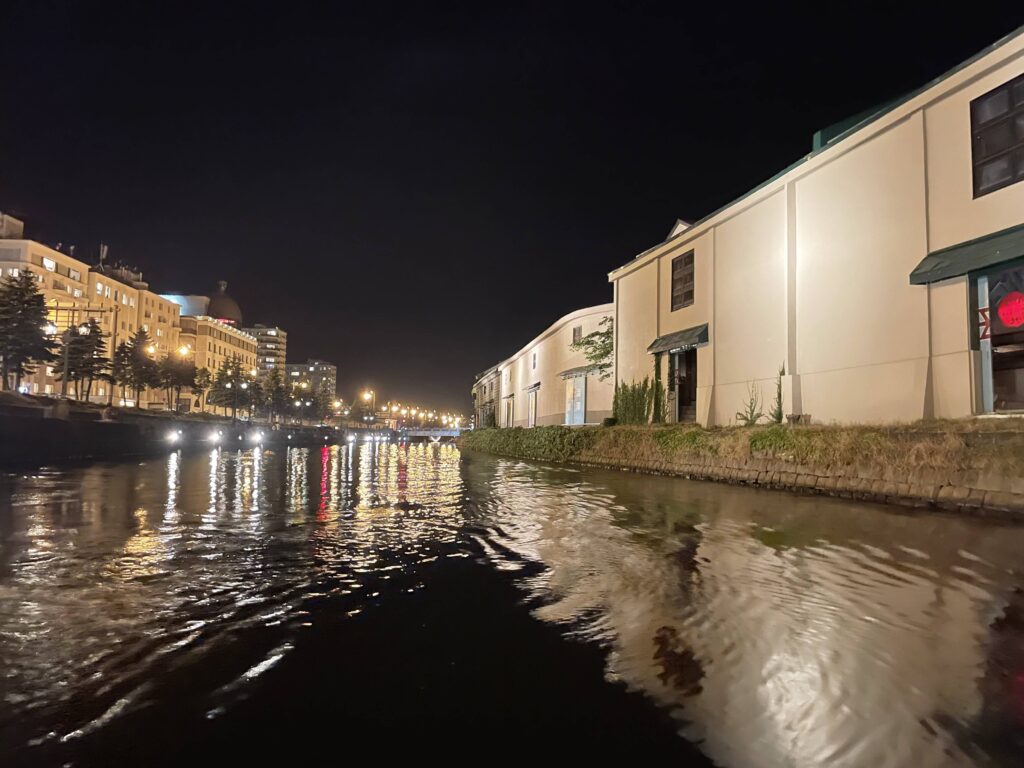 Buildings on both sides of the Otaru Canal glowing in the dark, their lights reflecting on the black water under the night sky.