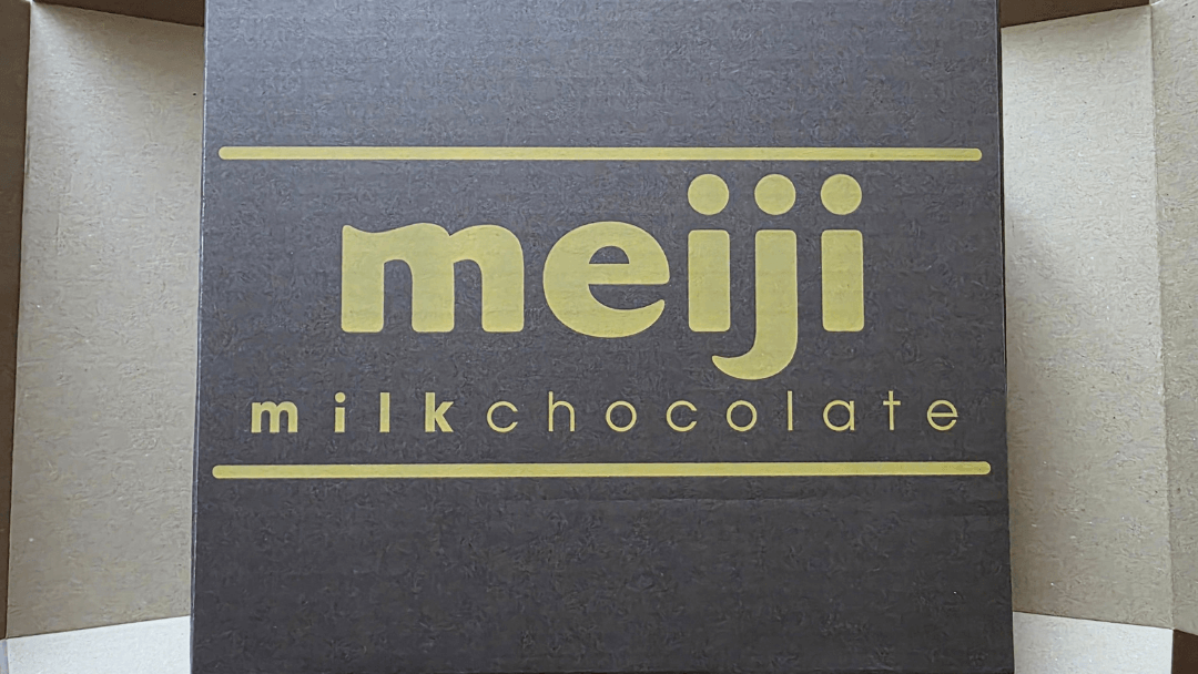 A Japanese shareholder benefit box from Meiji Co., Ltd. containing signature snacks and a yogurt gift voucher