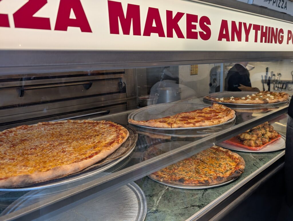 Display case filled with New York style pizza slices at Henry’s Pizza